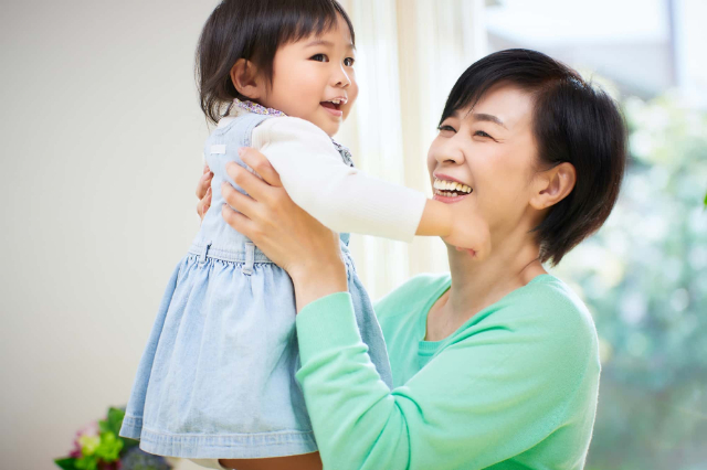前歯を入れ歯にした女性が孫を抱っこしているイメージ