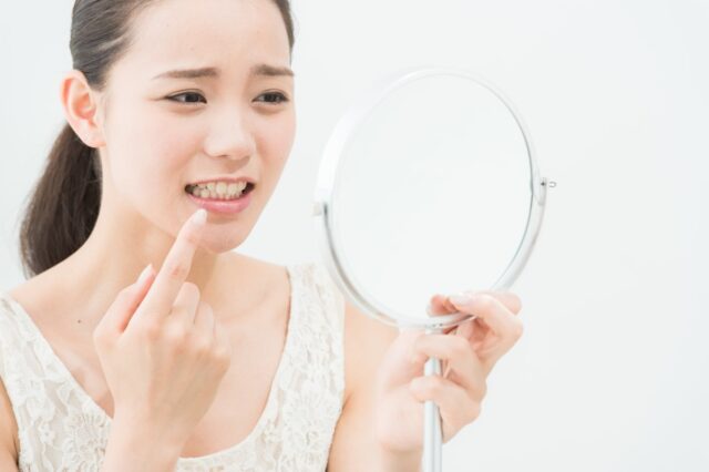 ホワイトニング後にしみる歯を顔をしかめて鏡で確認する女性