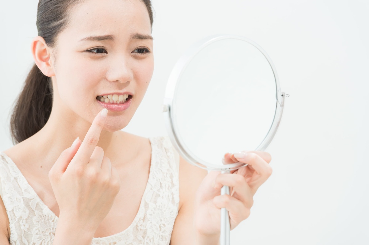 ホワイトニング後にしみる歯を顔をしかめて鏡で確認する女性