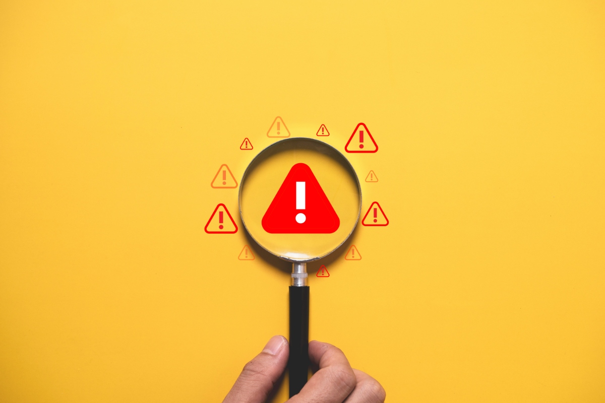 黄色の背景に赤いビックリマークを見る虫眼鏡